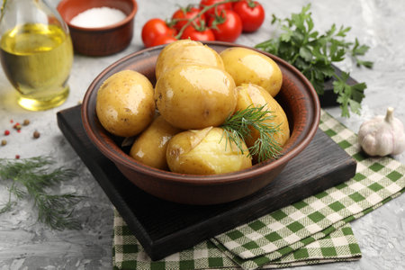 Tasty young boiled potatoes with dill, oil in bowl and products on gray textured table, closeupの写真素材