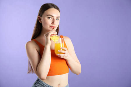 Woman drinking refreshing drink through straw on violet background, space for textの写真素材