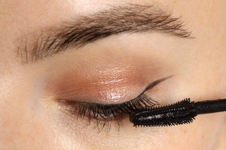 Woman applying mascara onto her eyelashes, closeup