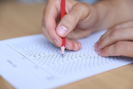 Student filling out multiple choice test at table, closeup. Passing examの写真素材