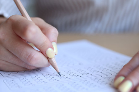Student filling out multiple choice test at table, closeup. Passing examの写真素材