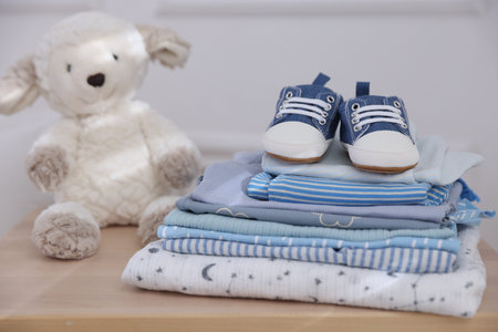 Stack of clean baby clothes, shoes and accessories on wooden table indoors, closeupの写真素材