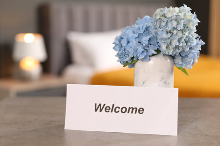 Card with word Welcome and hydrangea flowers on grey table indoorsの写真素材
