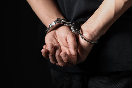 Man in metal handcuffs on black background, closeup