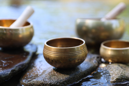 Tibetan singing bowls with mallets on stones in river, closeupの写真素材