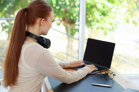 Teenage girl using laptop at wooden desk indoors. Home workplace