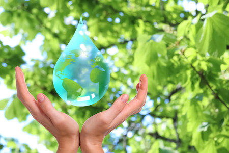 Drop with Earth inside falling into woman's hands against blurred green background