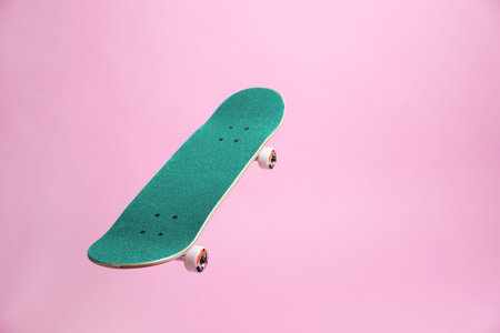 Turquoise skateboard in air against pink background.の写真素材