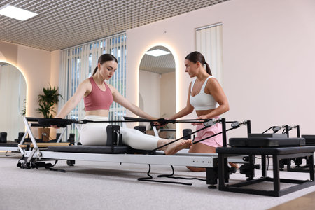 Woman exercising on reformer supervised by pilates instructor in studio