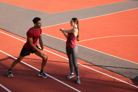 Smiling couple in sportswear doing warm-up exercises before run at stadium. Space for text