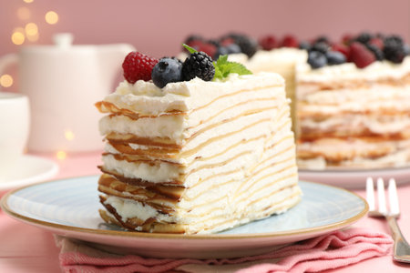Piece of tasty crepe cake with berries served on pink wooden table against blurred lights, closeup