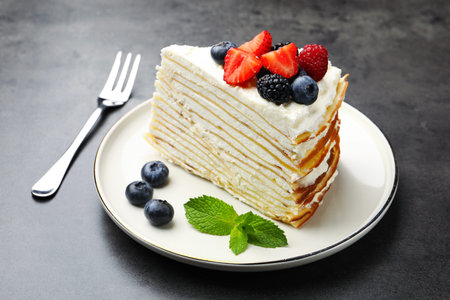 Piece of tasty crepe cake with berries served on gray table, closeup