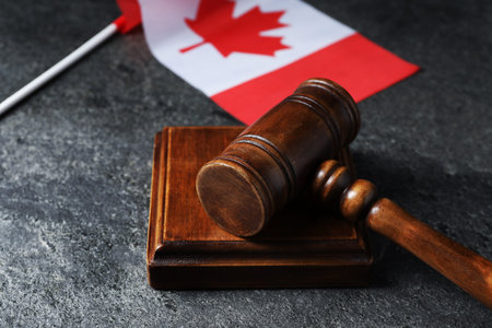 Judge's gavel and flag of Canada on gray table, closeup