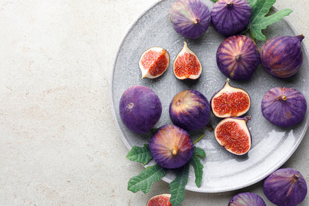 Fresh ripe figs and green leaves on gray textured table, flat lay. Space for text