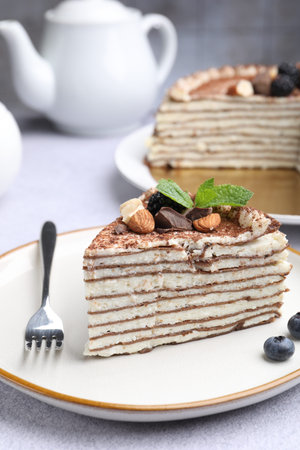 Piece of tasty crepe cake with cocoa powder, chocolate, nuts and blackberry served on light table,...