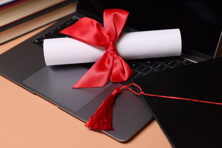 Diploma, laptop and books on beige table, closeup
