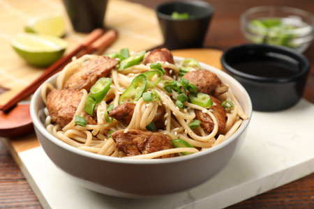 Tasty noodles with chicken, green peppers and sesame seeds served on wooden table, closeup