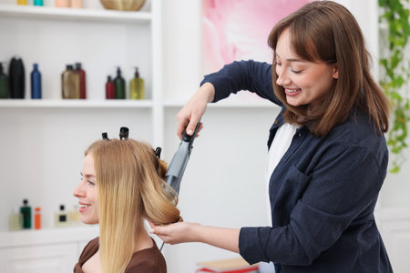 Professional hairstylist curling woman's hair in salonの写真素材