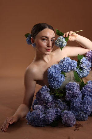 Beautiful young woman with hortensia flowers on brown background