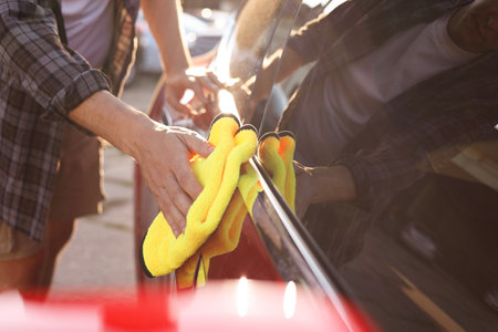 Man wiping car with yellow microfiber rag outdoors, closeupの写真素材