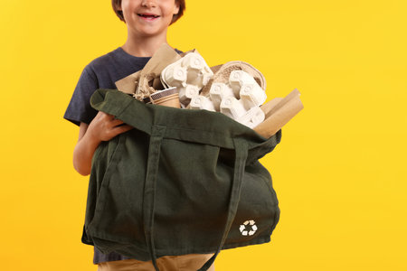 Cute little boy with bag full of different waste paper on orange background, closeup. Space for textの写真素材