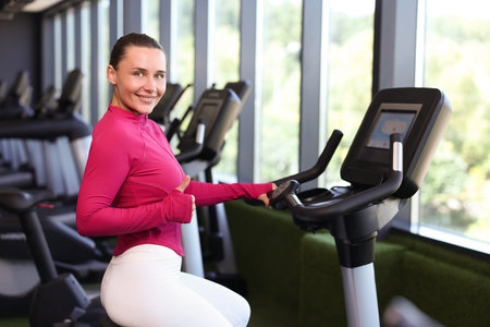 Smiling woman showing thumbs up on exercise bike in gym