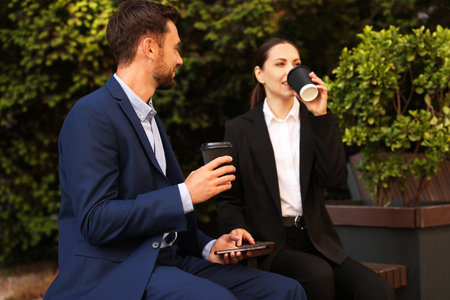 Coffee to go. Businesspeople with paper cups of drinks on bench outdoorsの写真素材