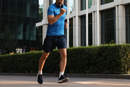 Man in sportswear running on city street, closeup. Space for textの写真素材