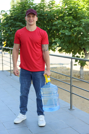 Smiling delivery man with cooler bottle of water near railings outdoorsの写真素材