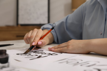 Calligraphy. Woman with brush writing phrase Keep Going on sheet of paper at table indoors, closeupの写真素材