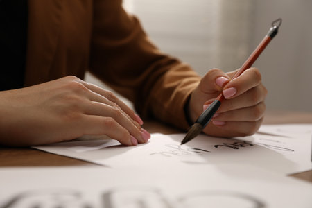 Calligraphy. Woman with brush writing phrase I Love You on sheet of paper at table, closeupの写真素材