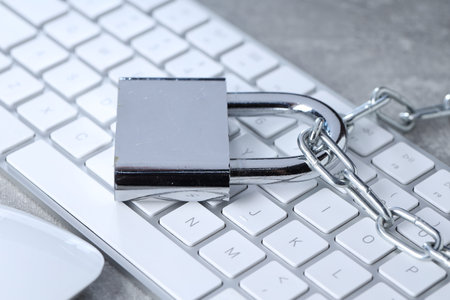 Cyber safety. Metal padlock, chain and computer keyboard on gray table, closeup