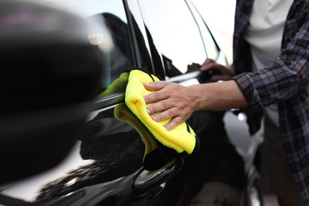 Man wiping car with yellow microfiber rag, closeup