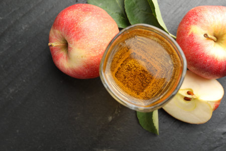 Fresh cider in glass, apples and green leaves on black table, flat lay. Space for text
