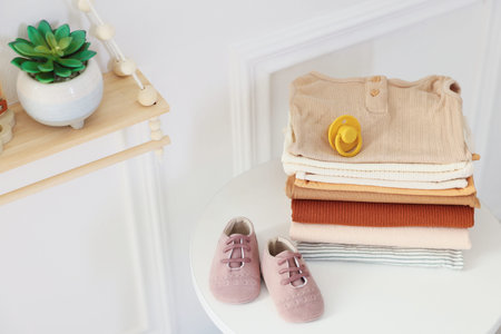 Stack of clean baby clothes and accessories on white table indoors, space for textの写真素材
