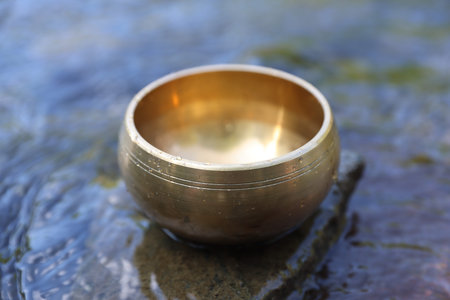 Tibetan singing bowl on stone in river, closeup