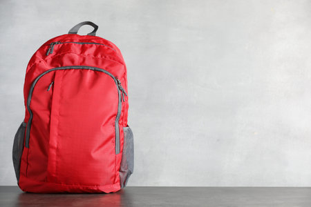 Red backpack on gray table against light background, space for text