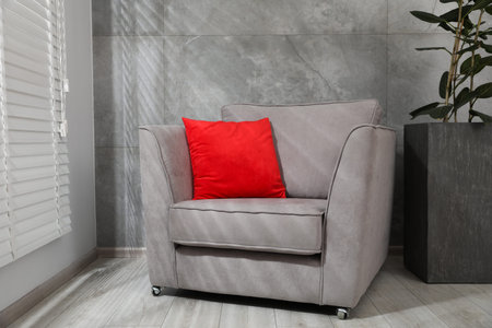 Comfortable armchair, red cushion and houseplant near gray marble wallの写真素材