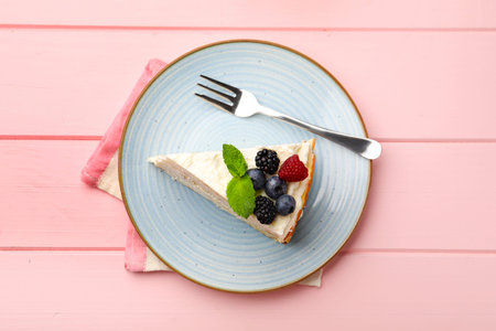 Piece of tasty crepe cake with berries served on pink wooden table, top view