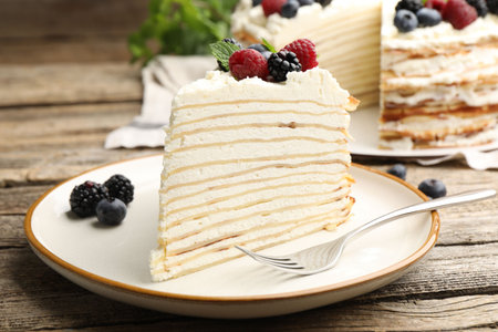 Piece of tasty crepe cake with berries served on wooden table, closeup
