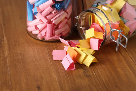 Colorful paper notes in glass jars on wooden table, closeup. Space for text