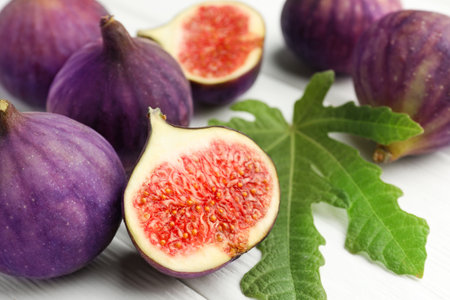 Fresh ripe figs and green leaf on white wooden table, closeup