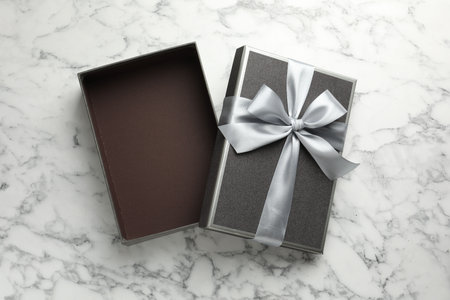 Opened gift box with beautiful lid on white marble table, top view