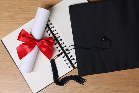 Graduation cap, diploma and notebook on wooden table, flat layの写真素材