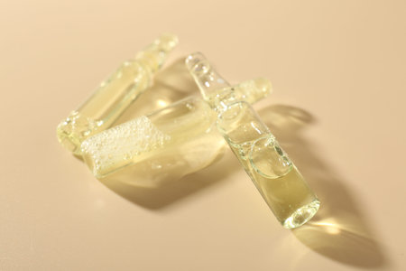 Glass ampoules with cosmetic product on beige background, closeup