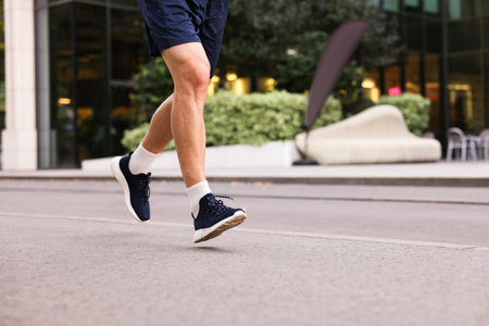 Man in stylish sneakers running outdoors, closeup. Space for text