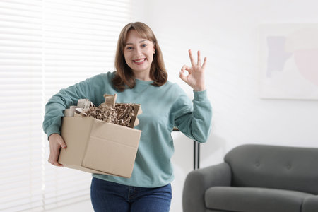 Recycling. Smiling woman holding cardboard box with different paper waste and showing OK gesture...