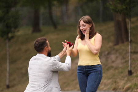Man with engagement ring making marriage proposal to his girlfriend outdoors