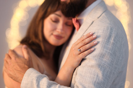 Making marriage proposal. Woman with engagement ring and her fiance hugging on light grey background, bokeh effectの写真素材
