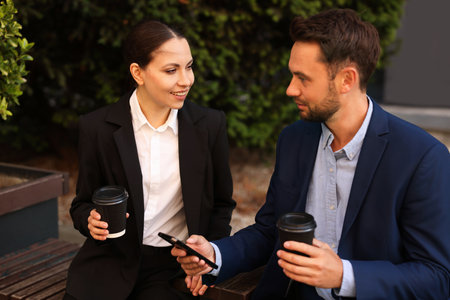 Coffee to go. Businesspeople with paper cups of drinks on bench outdoorsの写真素材